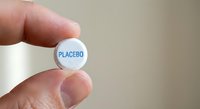 Hand holding white placebo pill tablet between fingers for medical research study and pharmaceutical testing concept.