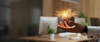 Businessman hand holding glowing light bulb with gear symbol, representing innovation, creative problem solving, and business strategy development in modern office environment.