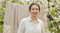 Happy middle-aged Caucasian woman in linen shirt standing near clothesline with blooming apple tree in spring garden for lifestyle and sustainable living.