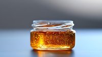 Fresh golden honey in glass jar with bubbles and natural crystallization showing pure raw sweetness and organic quality against blurred background.