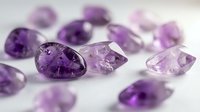 Collection of natural amethyst gemstones in various purple shades scattered on white surface for jewelry making and luxury accessories design projects.