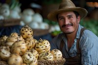 Hispanic farmer displaying fresh yellow spotted dragon fruit at local market stand, wearing straw hat and denim shirt, genuine smile while presenting exotic produce.