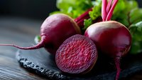 Fresh red beetroot with green leaves and cut half showing vibrant interior texture on black stone surface, natural food photography for healthy eating concept.