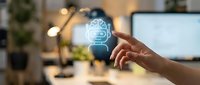 Human hand touching glowing brain hologram with circuit patterns in modern office workspace representing artificial intelligence and machine learning technology.