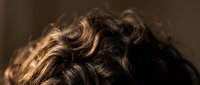 Close-up of wavy brown hair with golden highlights showing natural texture and movement against soft blurred background for beauty and haircare concepts.