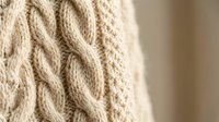 Close-up of cream cable knit sweater texture showing intricate braided pattern and soft wool fibers for cozy winter fashion and textile design.