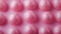Row of shiny pink spheres with glossy highlights arranged on matching pink background, suitable for abstract design, cosmetics packaging, beauty product promotion, and modern graphic projects.