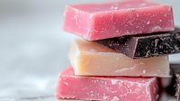 Handmade soap bars stacked in pink, beige, and dark brown colors with natural texture on neutral background for skincare and bath products.