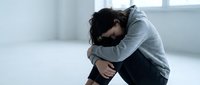 Young woman sitting alone on floor experiencing depression and mental health struggles in minimalist room with natural light for wellness concepts.