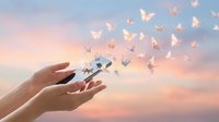 Hands releasing white paper butterflies into pastel sunset sky symbolizing freedom, transformation, hope and new beginnings for mental health and spiritual growth.