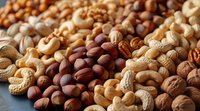 Mixed assortment of raw nuts and seeds including cashews, pecans, walnuts, hazelnuts and peanuts arranged on dark surface with selective focus.