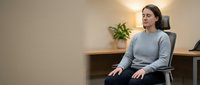 Young Caucasian woman in gray sweater sitting in modern office chair at wooden desk, professional workspace environment for business concepts.
