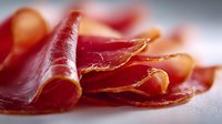 Thinly sliced cured ham prosciutto arranged on white surface, delicatessen meat for gourmet cooking and appetizers.