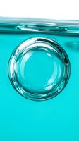 Transparent water bubble suspended in turquoise liquid with rippling surface above, ideal for skincare, cosmetics, wellness and beauty product packaging design.
