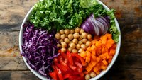 Colorful healthy Buddha bowl with fresh kale, purple cabbage, chickpeas, carrots, red peppers and onions on rustic wooden background for meal prep.