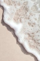 Gentle ocean foam washing onto beige sandy beach creates natural diagonal composition with white bubbles and soft waves meeting shoreline.