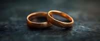 Two golden wedding bands on dark textured surface with soft focus and warm highlights, symbolizing marriage, commitment and eternal love in minimalist composition.