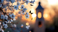 Delicate white cherry blossoms against sunset sky with church steeple silhouette and flying birds creating romantic spring atmosphere. Soft bokeh background adds dreamy mood.