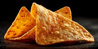 Crispy golden tortilla chips with textured surface on dark background, perfect snack food for parties, appetizers and Mexican cuisine presentations.