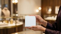 Businessman holding blank white box in luxury retail environment with warm lighting and blurred store background for product packaging mockup.