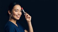 Young Asian woman applying red lipstick with smile on dark background. Beauty makeup routine and cosmetics concept for advertising campaigns.