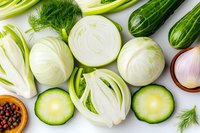 Fresh sliced fennel bulbs, cucumber rounds, and onion on white background with dill and peppercorns, arranged in flat lay composition for food photography.