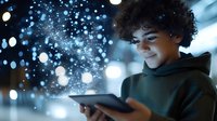 Young African American teen in hoodie using digital tablet with magical glowing particles and bokeh lights emerging from screen, creating ethereal night atmosphere.