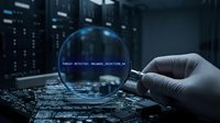 Gloved hand holding magnifying glass over circuit board with threat detection alert displayed in lens, cybersecurity concept for malware analysis and digital protection systems.
