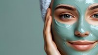 Close up of woman with mint green clay mask on face smiling gently, showing clean fresh skin and natural beauty during spa skincare treatment routine.