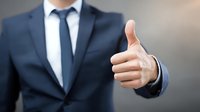 Businessman in navy suit showing thumbs up gesture, representing approval, success, and positive feedback in corporate environment.