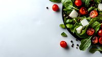 Fresh Mediterranean salad with mozzarella, cherry tomatoes and baby spinach leaves on black plate against white background, copy space for menu or recipe.