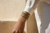 Elegant stacked gold and green bracelets on woman's wrist against white clothing and neutral background, perfect for jewelry advertising.