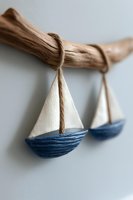 Decorative sailboat ornaments in white and blue hanging on driftwood branch against light background, creating coastal nautical home decor atmosphere.