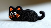 Cute black cat embroidered patch with orange details and curled tail lying on white fabric. Decorative handmade accessory for clothing customization.