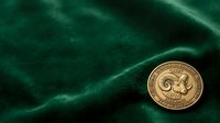 Antique gold coin with ornate design resting on rich emerald green velvet fabric, suitable for numismatic, luxury, and collectible asset photography.