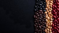 Colorful rows of dried beans including red kidney, black, and pinto beans on dark background with copy space, macro food photography for healthy eating concept.