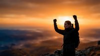 Male hiker celebrating success on mountain peak at golden sunset with raised arms, adventure achievement concept for motivational content.