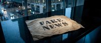 Crumpled newspaper with fake news headline lying on dark surface in modern office environment with city lights background.