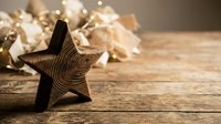 Wooden star decoration with warm bokeh lights and gift boxes on rustic table creating cozy holiday atmosphere for seasonal celebrations and home decor.