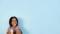 Young girl with dark hair and medium skin tone smiling against light blue background, wearing patterned shirt. Suitable for education, childcare, family and diversity concepts.