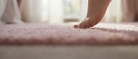 Woman's hand touching soft pink textured carpet in bright home interior for flooring and comfort concepts.
