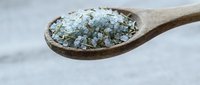 Coarse sea salt crystals in wooden spoon on white marble surface for cooking seasoning and culinary preparation in kitchen.