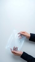 Female hands holding transparent plastic packaging against white background, showcasing product display and unboxing experience for retail and e-commerce.