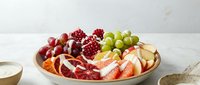 Fresh fruit platter with grapes, strawberries, pomegranate seeds and sliced apples arranged on wooden board for healthy snacking and entertaining.