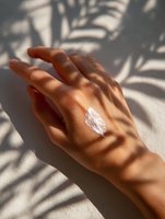 Female hand with moisturizing cream and palm leaf shadows on light background, demonstrating skincare product application in natural sunlight.