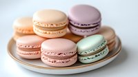 Pastel colored French macarons with delicate almond meringue shells and creamy filling arranged on white porcelain plate with gold trim. Sweet dessert photography.