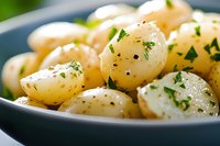 Fresh boiled baby potatoes seasoned with herbs, black pepper and parsley served in dark bowl, close up view of homemade side dish with selective focus.