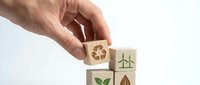 Hand arranging wooden blocks with green eco symbols including recycling, wind turbines, leaves and trees representing sustainable business practices.