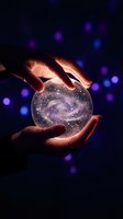 Hands holding glowing crystal ball with galaxy inside against dark background with purple bokeh lights for mystical and spiritual concepts.