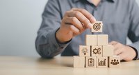 Businessman placing wooden block with target icon on pyramid of business strategy blocks representing goal achievement and success planning.